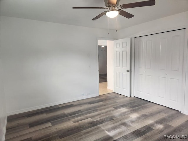 unfurnished bedroom with ceiling fan, a closet, and dark wood-type flooring