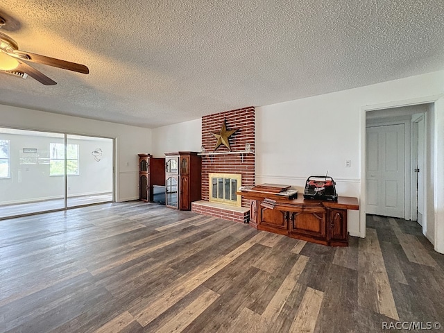 living room featuring a brick fireplace, ceiling fan, a textured ceiling, and dark wood-type flooring