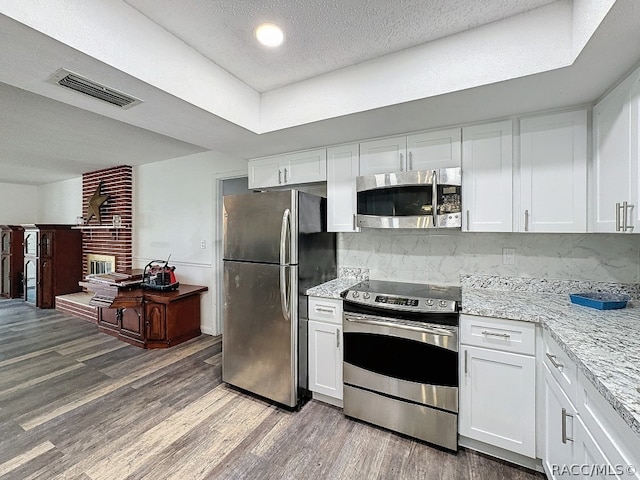 kitchen with white cabinets, appliances with stainless steel finishes, tasteful backsplash, and hardwood / wood-style floors