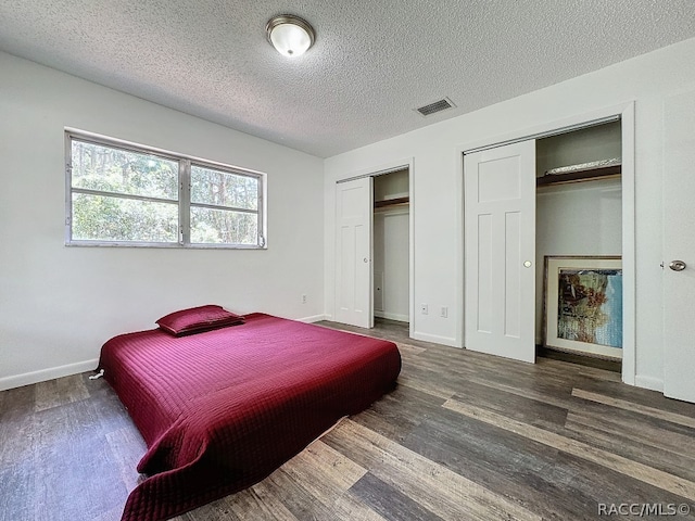 bedroom featuring two closets, a textured ceiling, and dark hardwood / wood-style floors