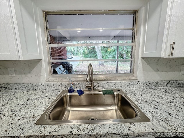 room details with white cabinets, light stone counters, and sink