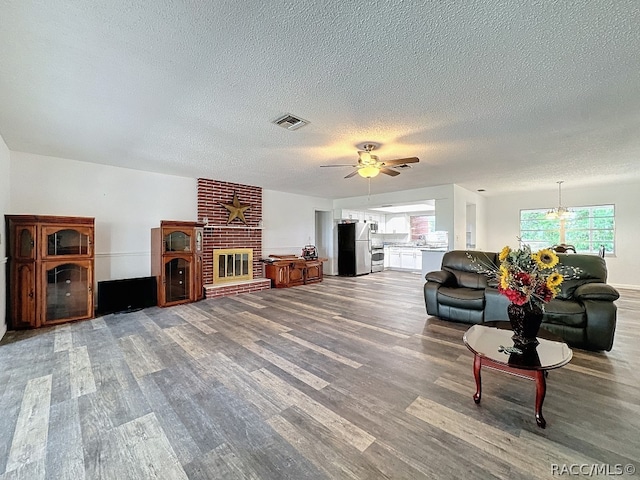 living room with wood-type flooring, a textured ceiling, a brick fireplace, and ceiling fan