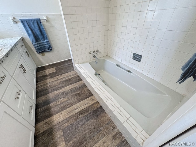 bathroom with tiled shower / bath, wood-type flooring, vanity, and tile walls