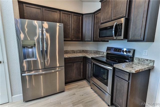 kitchen featuring dark brown cabinetry, light wood-type flooring, light stone countertops, and appliances with stainless steel finishes