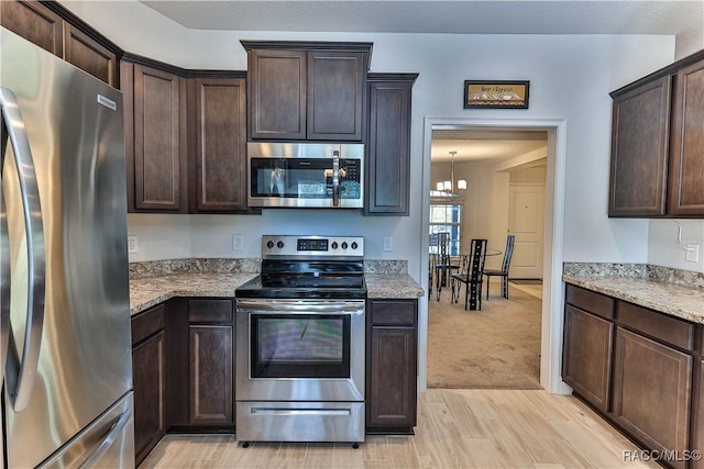 kitchen featuring appliances with stainless steel finishes, a chandelier, dark brown cabinetry, light stone countertops, and light carpet