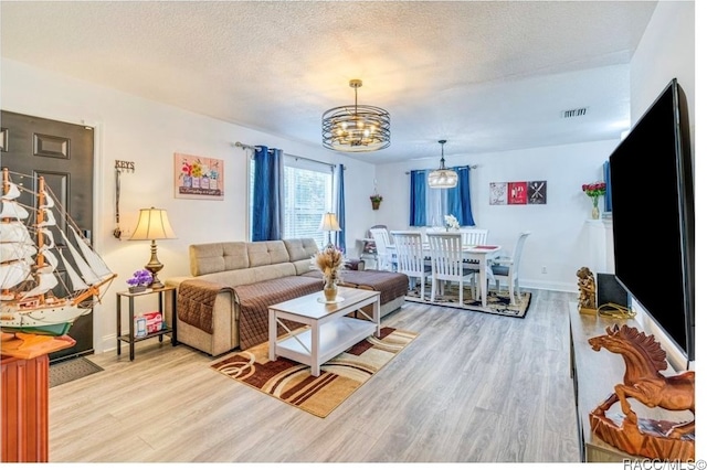 living room with a textured ceiling, light hardwood / wood-style floors, and an inviting chandelier