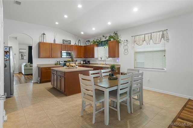 kitchen with appliances with stainless steel finishes, sink, light tile patterned floors, a center island, and lofted ceiling