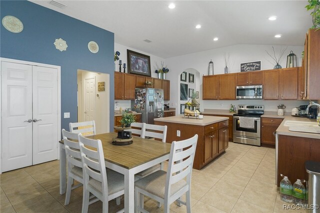 kitchen with appliances with stainless steel finishes, vaulted ceiling, sink, a kitchen island, and light tile patterned flooring