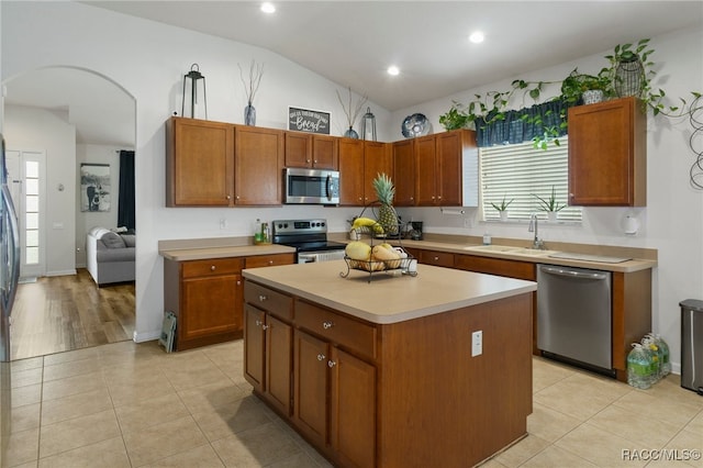 kitchen with appliances with stainless steel finishes, sink, light tile patterned floors, a center island, and lofted ceiling