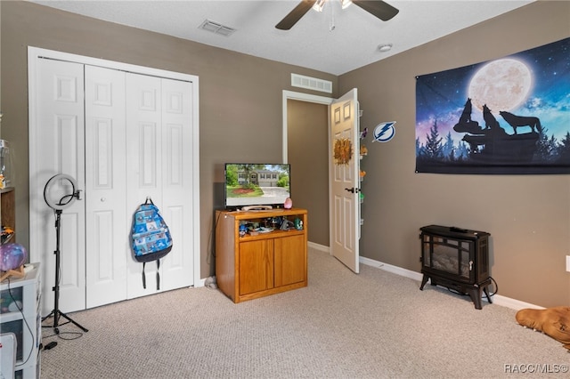 interior space with ceiling fan, light colored carpet, and a wood stove