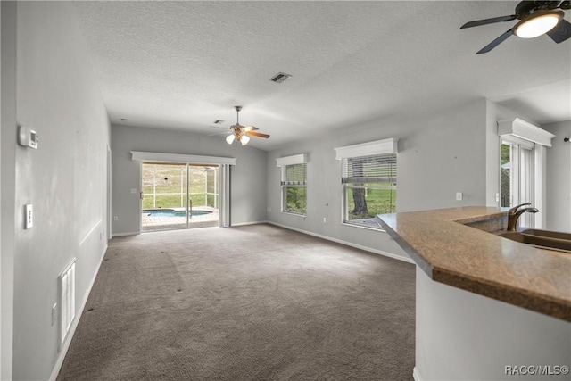unfurnished living room featuring ceiling fan, visible vents, a sink, and carpet