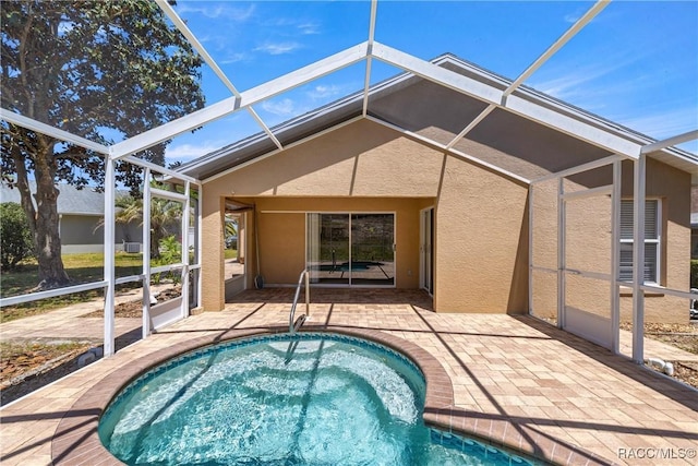 rear view of house with a lanai, stucco siding, a hot tub, and a patio area