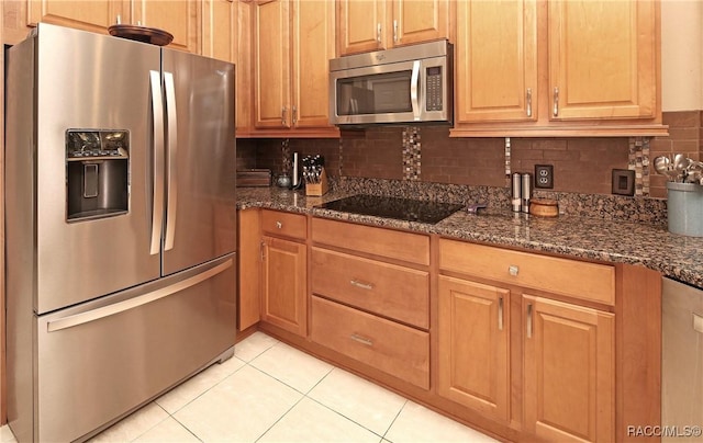 kitchen featuring light tile patterned flooring, backsplash, appliances with stainless steel finishes, and dark stone counters