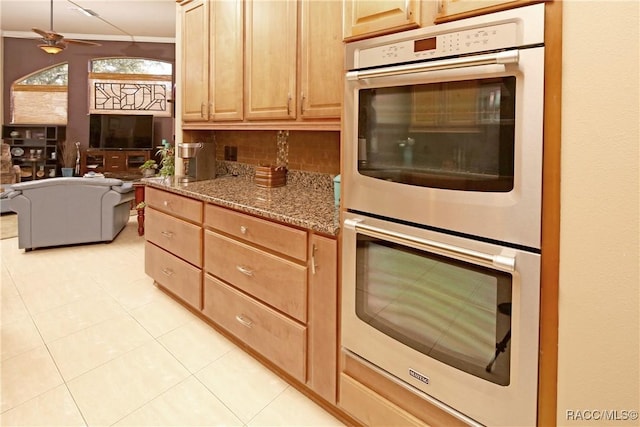 kitchen featuring ceiling fan, light brown cabinets, double oven, dark stone countertops, and light tile patterned flooring