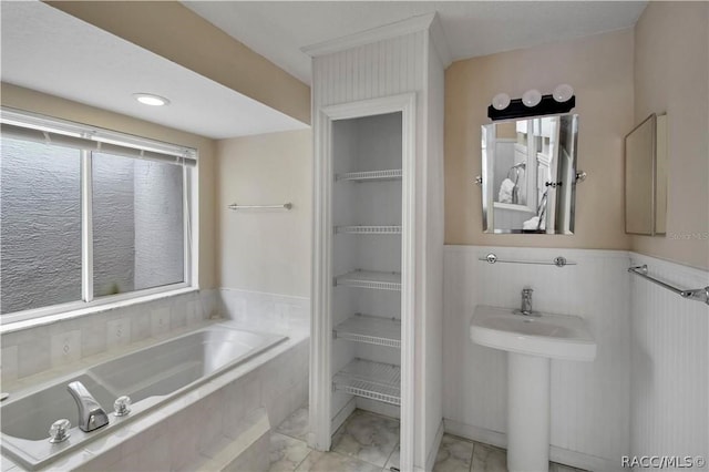 bathroom with built in shelves, plenty of natural light, and a relaxing tiled tub