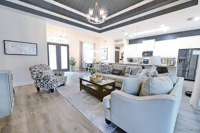 living area featuring french doors, a raised ceiling, visible vents, light wood-style floors, and a chandelier