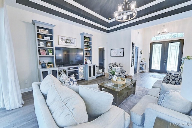 living room featuring a chandelier, wood finished floors, baseboards, french doors, and a raised ceiling