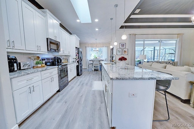 kitchen with appliances with stainless steel finishes, white cabinets, a sink, and a kitchen bar