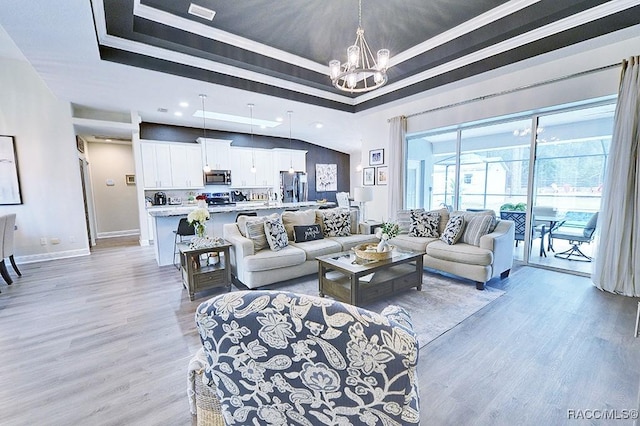 living room featuring light wood-style floors, a raised ceiling, a chandelier, and baseboards