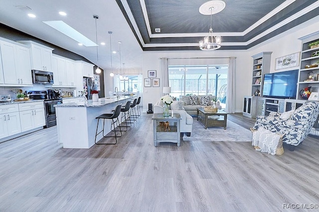 living area featuring baseboards, built in features, an inviting chandelier, a tray ceiling, and light wood-type flooring