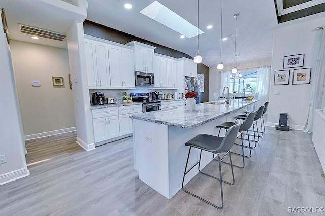 kitchen with visible vents, appliances with stainless steel finishes, white cabinets, a sink, and a large island with sink