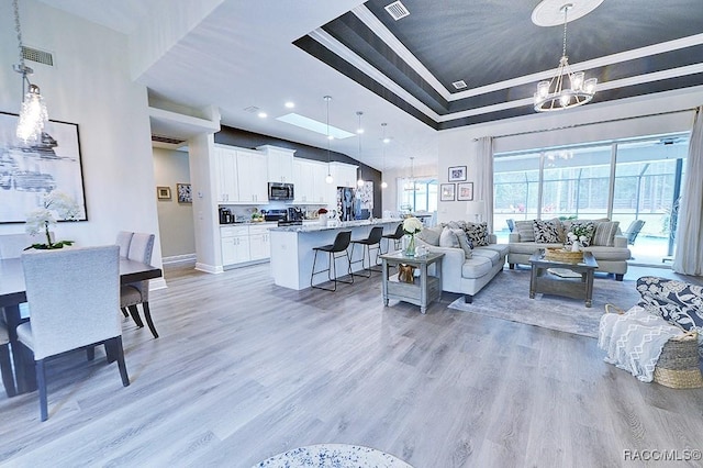 living room with a tray ceiling, visible vents, a chandelier, light wood-type flooring, and baseboards