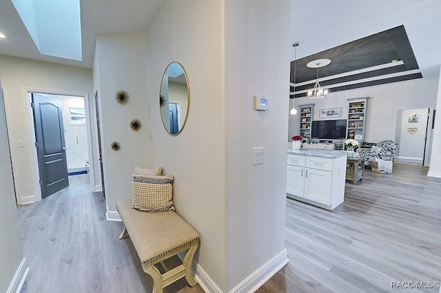 corridor with a tray ceiling, light wood-type flooring, and baseboards