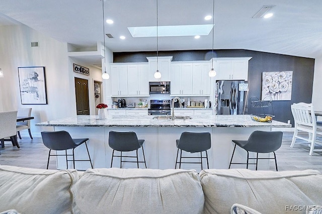 kitchen featuring stainless steel appliances, a breakfast bar, a sink, and white cabinets