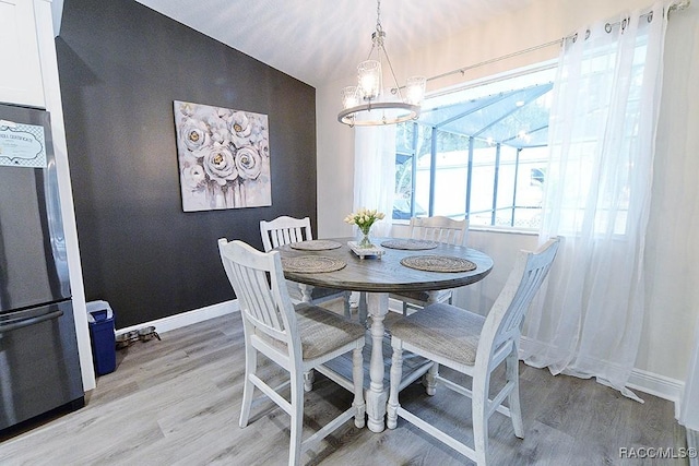 dining space featuring lofted ceiling, light wood-style flooring, baseboards, and a notable chandelier