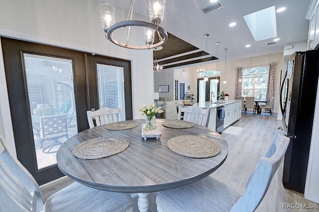 dining room featuring a skylight, french doors, visible vents, an inviting chandelier, and light wood-style floors