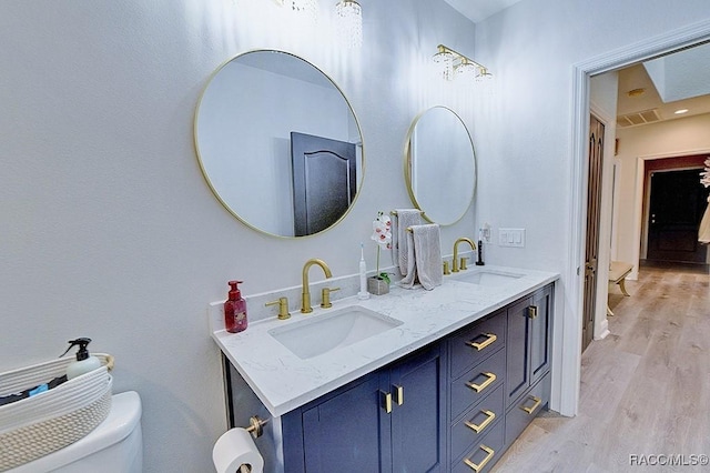 full bath with double vanity, visible vents, a sink, and wood finished floors