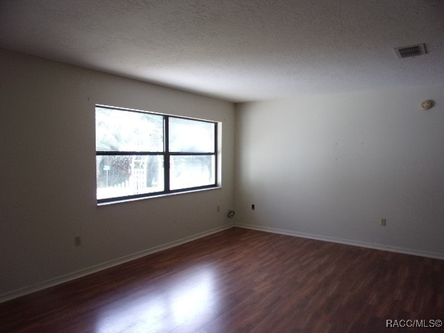 empty room with a textured ceiling and dark wood-type flooring