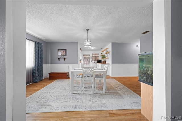 dining space featuring a notable chandelier, a textured ceiling, and light hardwood / wood-style flooring