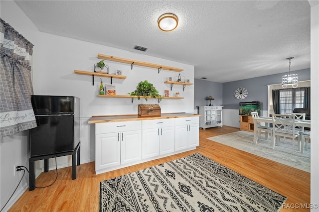 kitchen featuring black fridge, a textured ceiling, decorative light fixtures, light hardwood / wood-style floors, and white cabinetry