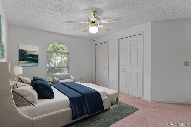 carpeted bedroom with two closets, ceiling fan, and a textured ceiling