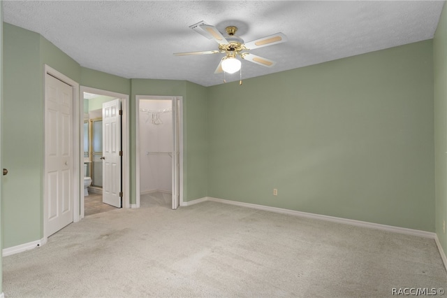 unfurnished bedroom with light carpet, a walk in closet, ceiling fan, a textured ceiling, and a closet