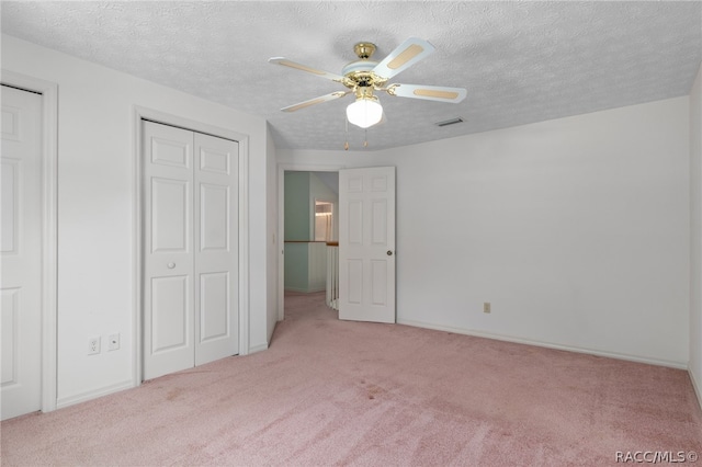 unfurnished bedroom featuring multiple closets, ceiling fan, light carpet, and a textured ceiling