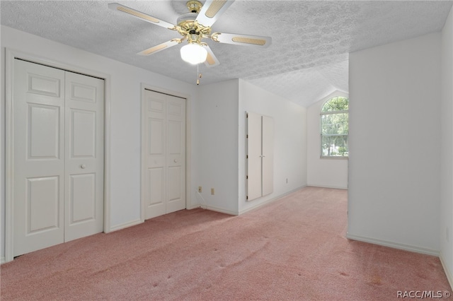 unfurnished bedroom with ceiling fan, vaulted ceiling, light carpet, and multiple closets