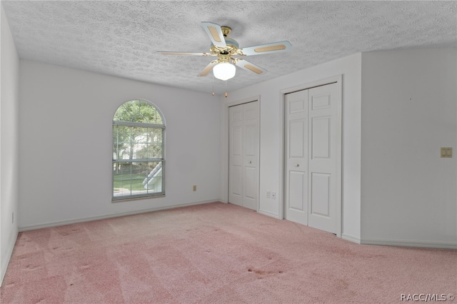 unfurnished bedroom with a textured ceiling, light colored carpet, ceiling fan, and multiple closets