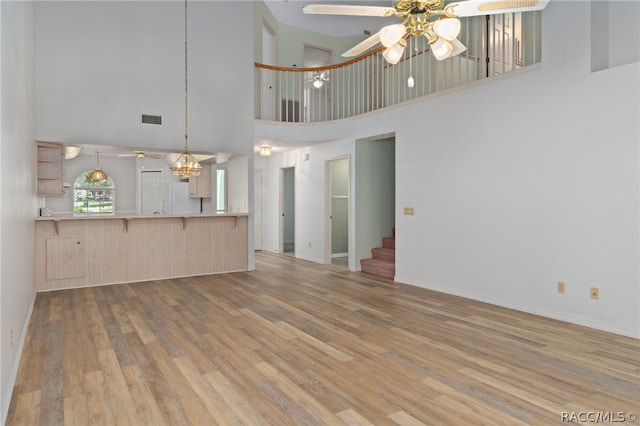 unfurnished living room featuring ceiling fan, light hardwood / wood-style floors, and a towering ceiling