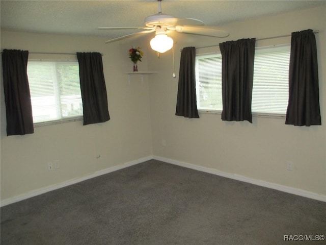 spare room featuring dark colored carpet, a healthy amount of sunlight, and baseboards