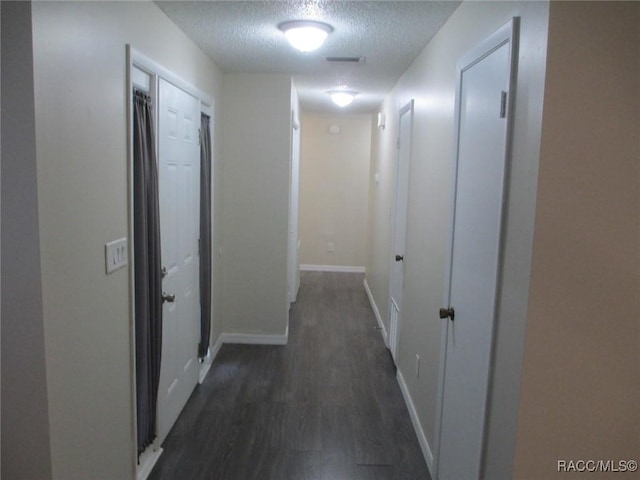 hall featuring a textured ceiling, dark wood-style flooring, and baseboards