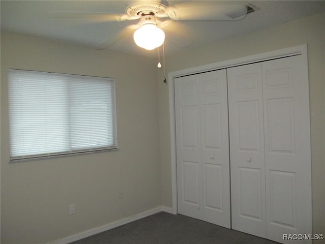 unfurnished bedroom with ceiling fan, baseboards, dark carpet, and a closet