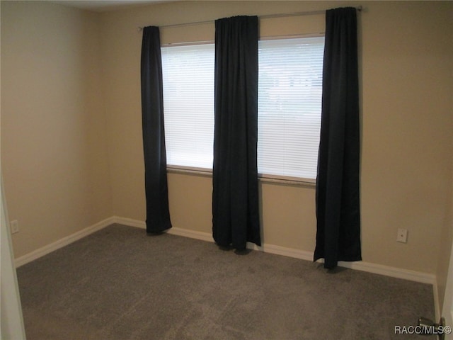 spare room featuring baseboards and dark colored carpet