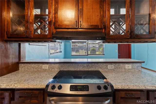 kitchen featuring light stone countertops, stainless steel stove, and range hood