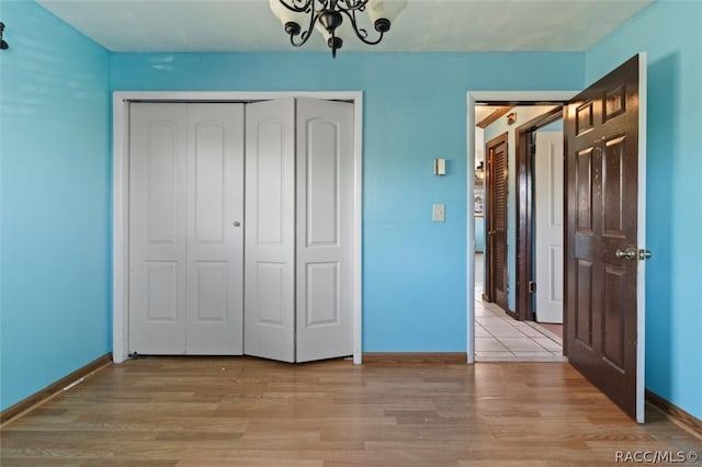 unfurnished bedroom featuring a chandelier, light wood-type flooring, and a closet