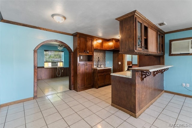 kitchen featuring kitchen peninsula, a kitchen bar, cooling unit, wooden walls, and crown molding