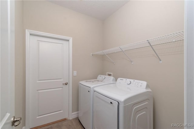 clothes washing area with washing machine and dryer and light hardwood / wood-style flooring