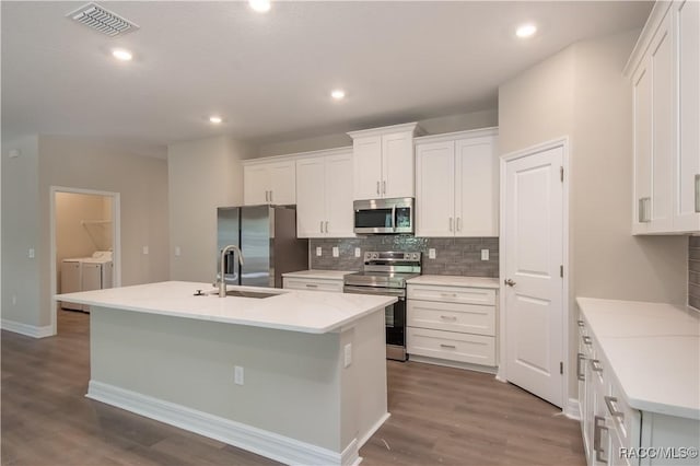 kitchen with white cabinets, appliances with stainless steel finishes, an island with sink, and washing machine and clothes dryer