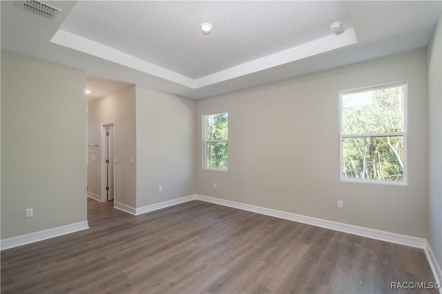 unfurnished room with dark hardwood / wood-style floors, a textured ceiling, and a tray ceiling